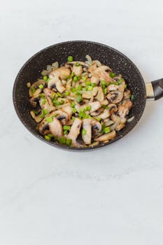 Sliced mushrooms sautéed with green onions in a frying pan. Perfect for healthy meals.