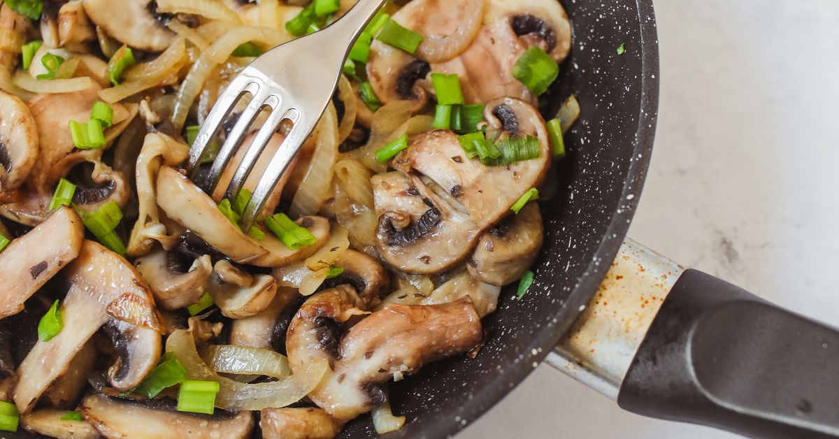 Cooked sliced mushrooms with herbs being lifted from a pan with a fork