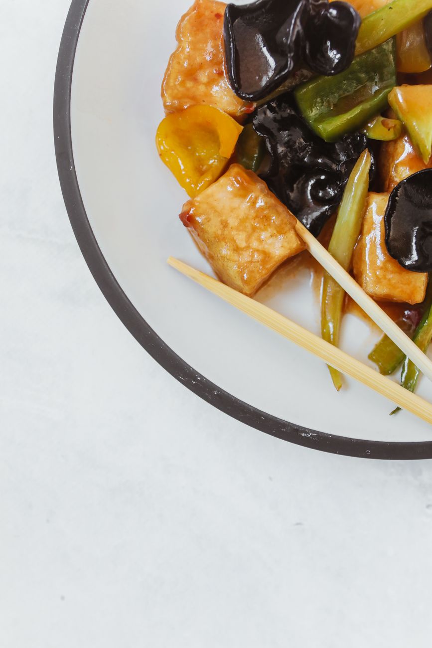 Cubes of silky tofu and diced mushrooms glistening in a glossy brick-red sauce, topped with sliced green scallions in a white ceramic bowl