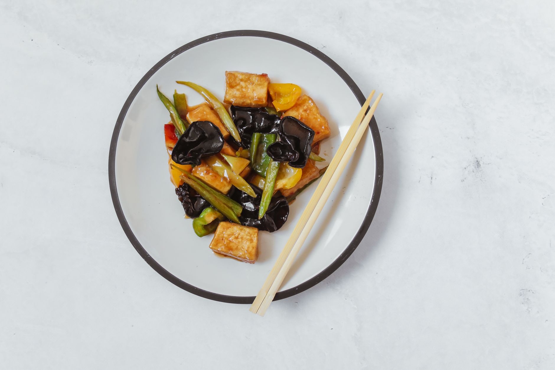 Top view of a vegan Asian dish with tofu, vegetables, and chopsticks on a white plate.