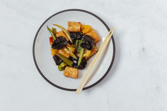 Golden tofu cubes with black wood ear mushrooms, green beans and peppers on a white plate