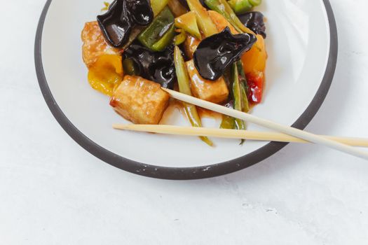 白色盘子上翻炒的美味豆腐与蔬菜特写镜头，非常适合美食摄影