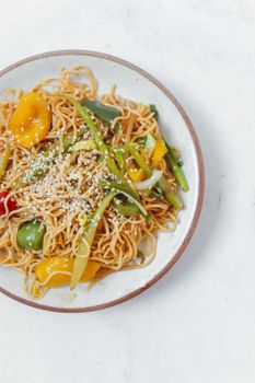 白色的盘子里盛着美味的炒面，配着鲜艳的蔬菜和芝麻