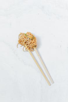 Close-up of noodles held by chopsticks on a marble background, perfect for Asian cuisine presentations.