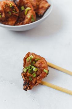 浅色背景上，用筷子夹着的辛辣亚洲饺子特写，以葱装饰