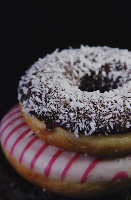 High angle of delicious doughnuts with glaze and coconut shavings placed against black background