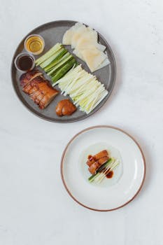 A flat lay of Peking duck with classic sides on a minimalist table setting.