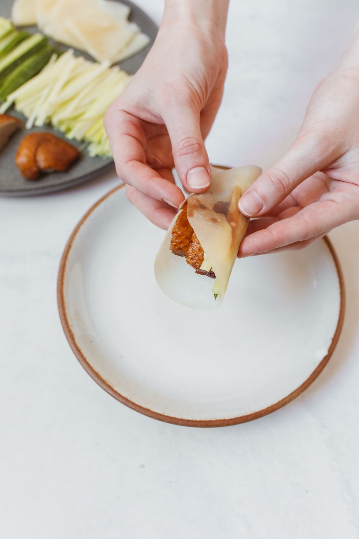 Hands wrapping crispy sliced Peking duck, cucumber matchsticks and spring onion in a thin Mandarin pancake with a smear of hoisin sauce.