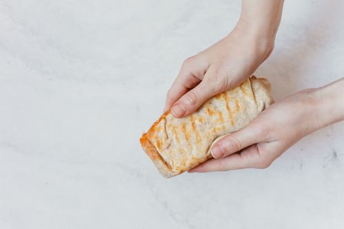 Free Close-up of hands holding a freshly made burrito with grill marks, ready to eat. Stock Photo