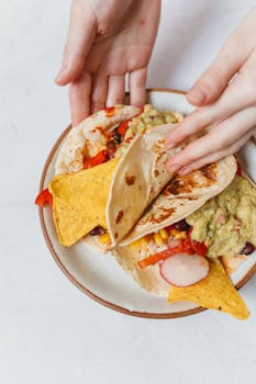 A close-up view of colorful tacos with guacamole and nachos on a plate, being held by hands.
