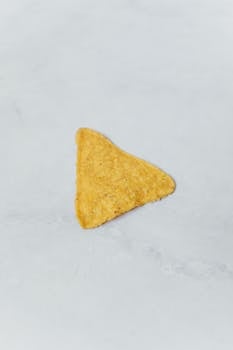 Close-up of a single triangular tortilla chip on a gray surface.