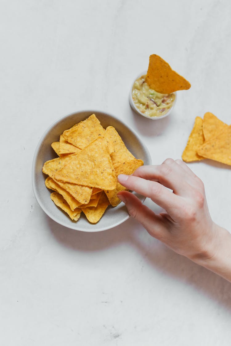 Person Picking Nachos From A Ceramic Bowl 