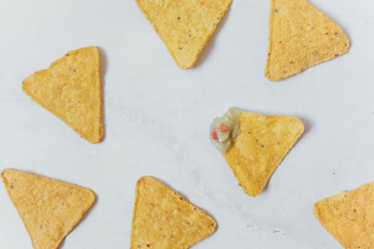 Flat lay of crunchy tortilla chips with guacamole on a white surface, perfect snack idea.
