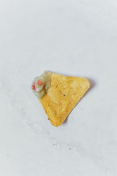 A close-up of a tortilla chip with guacamole dip on a white background, perfect for food themes.