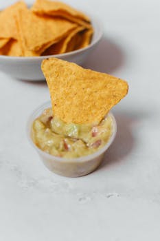 Close-up of crunchy tortilla chip with creamy guacamole, perfect for Mexican cuisine lovers.