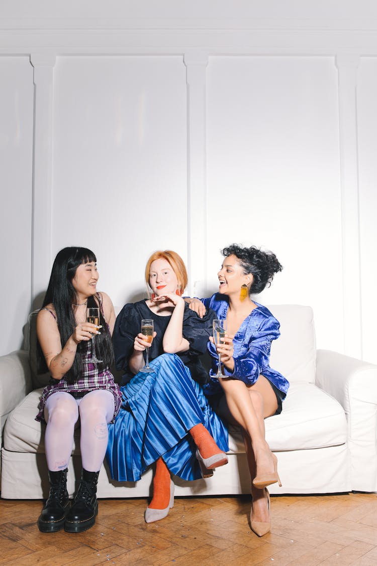 Three Women Sitting On White Couch Holding Glasses Of Wine