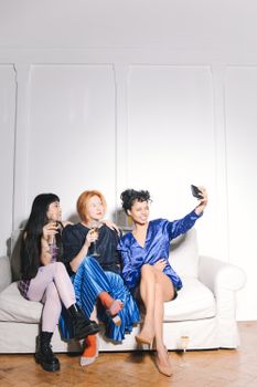 三位性格各异的女性在室内沙发上自拍、享用饮料，展现着友谊与休闲时光