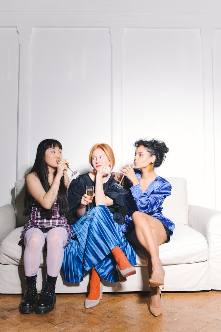 Three Women Sitting On White Couch Drinking Wine