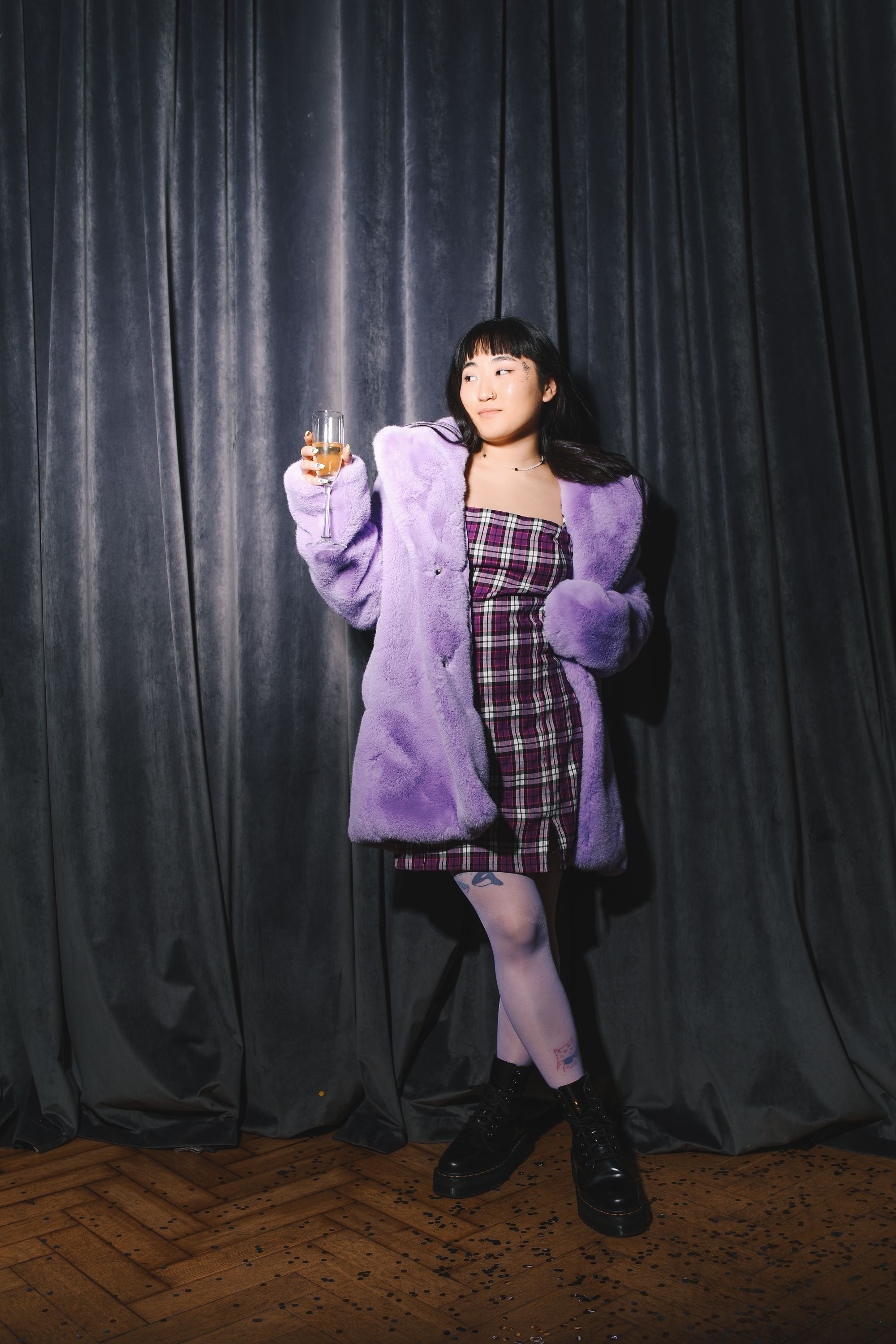 一位穿着紫色外套和格子连衣裙的时髦亚洲妇女，在聚会上拿着一个酒杯