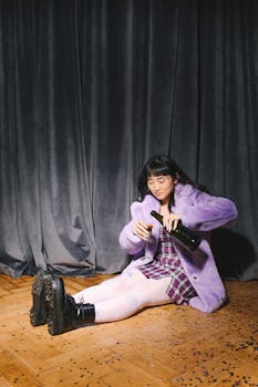 一位时尚女子身穿紫色服装，坐在室内的镶木地板上倒酒