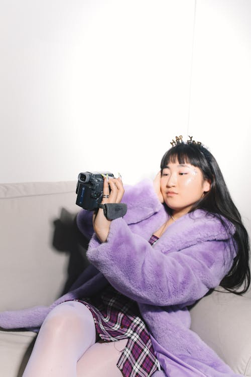 Young Woman Sitting on a Sofa and Filming with a Vintage Camcorder 