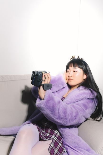 Young woman in vibrant retro fashion holding a camcorder indoors, capturing moments.