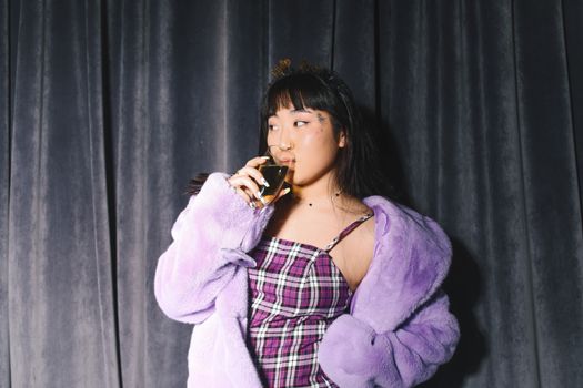 一位穿着时尚服装的女性在室内以窗帘为背景喝着饮料