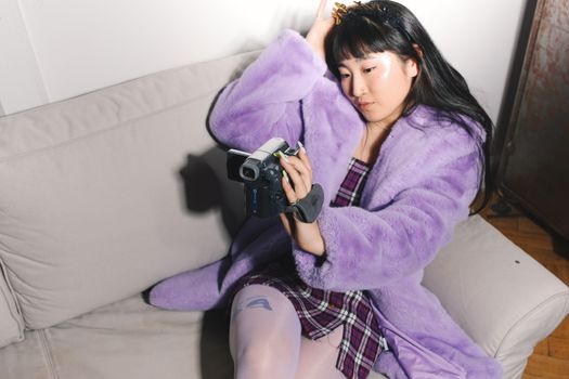一位穿着紫色外套的年轻女子正用相机对着沙发上的自己拍照，画面现代时尚