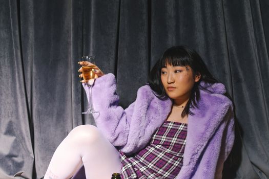 派对上，一位穿着紫色外套、端着酒杯的时尚亚洲女性
