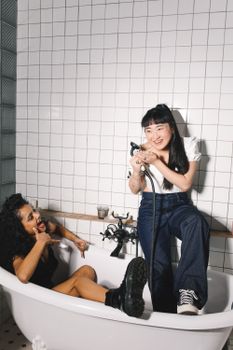 两个女人在室内的浴缸里欢笑玩耍，展现着友谊和欢乐