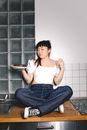一位年轻女子随意地坐在厨房柜台上，手里拿着美味的蛋糕