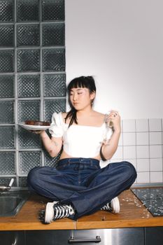 一位年轻女子随意地坐在厨房柜台上，手里拿着美味的蛋糕