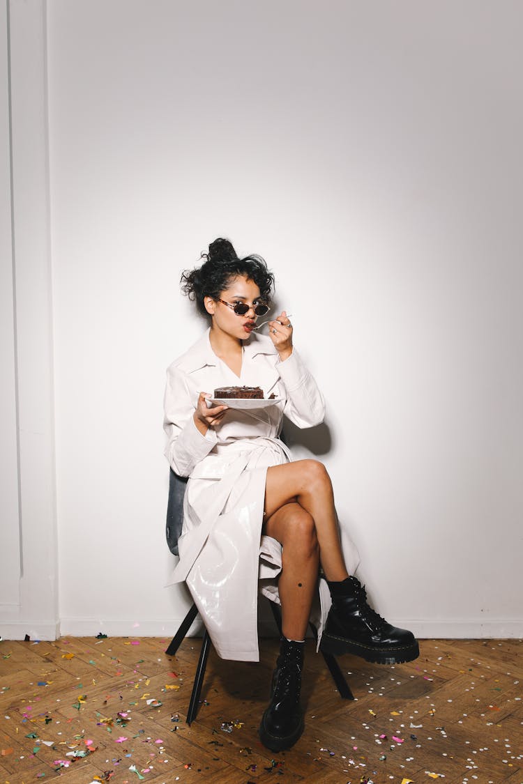 Woman Wearing A White Coat And Black Boots Eating A Chocolate Cake