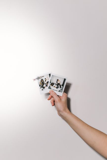Close-up of a hand holding polaroid photos on a white background. Minimalist design with copyspace.