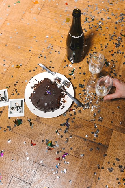 Celebratory scene with chocolate cake, champagne bottle, glasses, and confetti on wooden flooring.