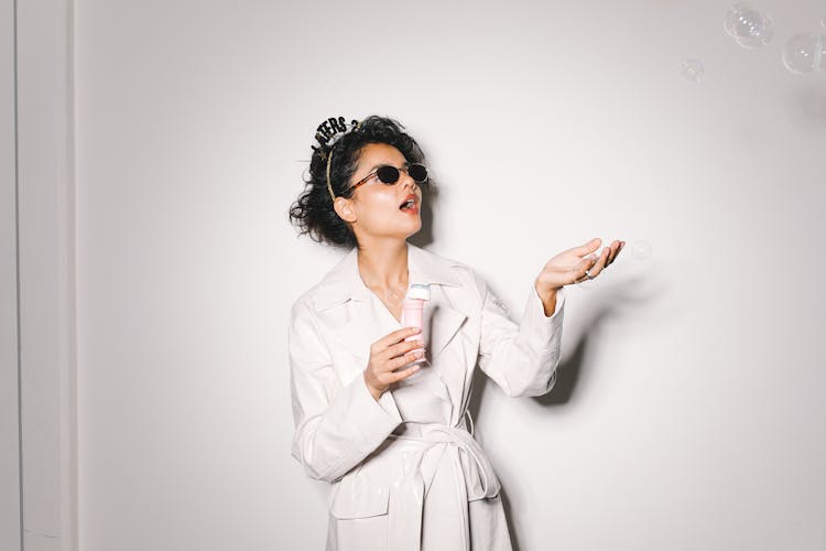 Young Woman In A White Trench Coat Blowing Soap Bubbles At A New Years Eve Party