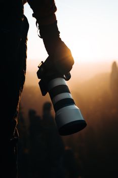 A silhouette of a photographer holding a DSLR camera at sunset, capturing the serene landscape.