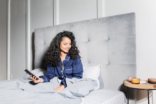 Woman in pajamas relaxing in bed with a smartphone, enjoying a cozy morning at home.