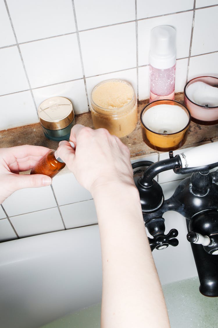 Hands Of A Person Holding A Bottle Of Body Product Near Candles