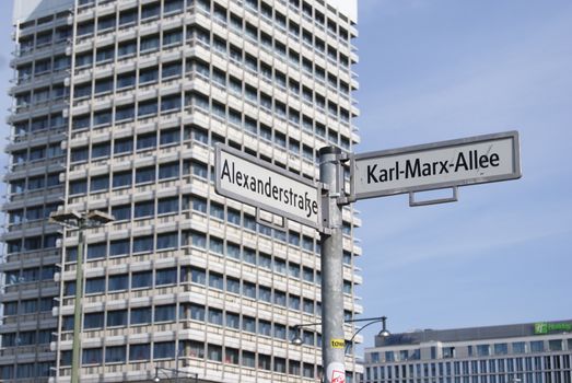 Street signs for Alexanderstraße and Karl-Marx-Allee with a highrise in Berlin.