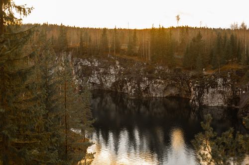 Free Serene autumn landscape featuring a tranquil lake surrounded by evergreen trees and rocky cliffs. Stock Photo