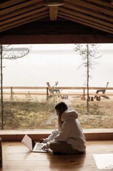 一名妇女在俯瞰宁静湖畔景色的舒适木屋里远程工作