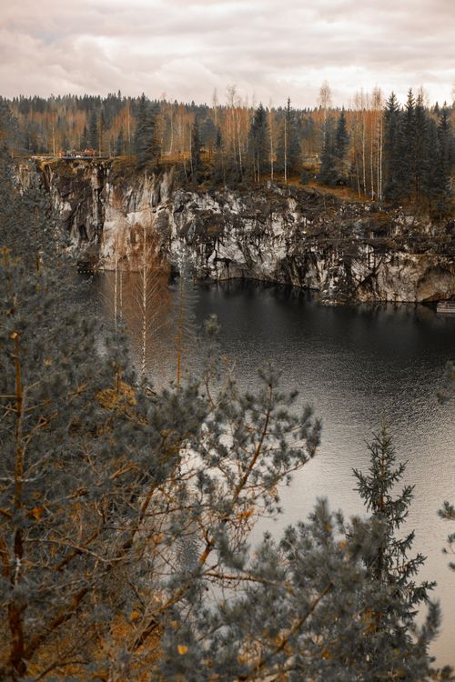 Free Tranquil autumn landscape with a serene lake and tall pine trees under a cloudy sky. Stock Photo