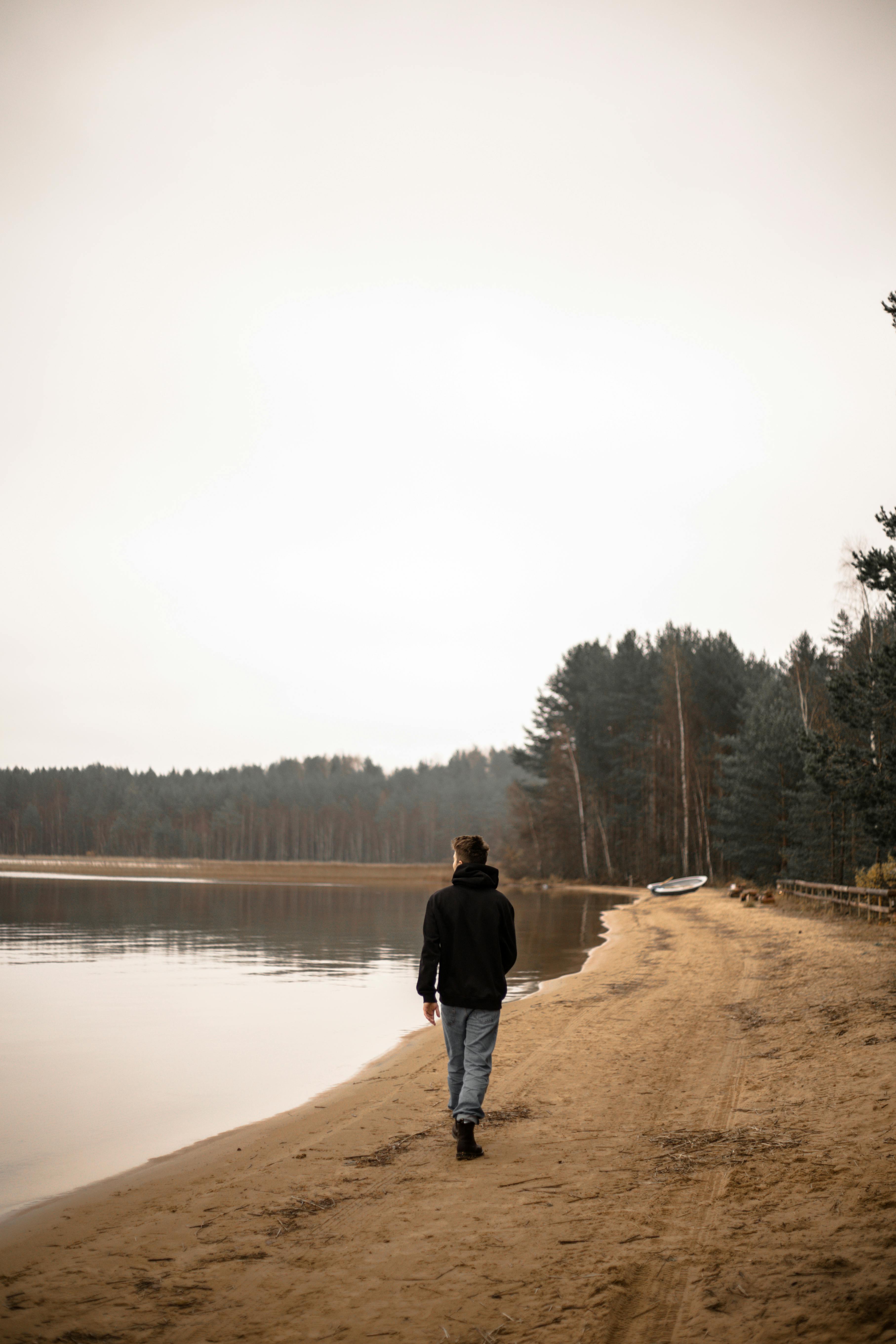 man in black jacket walking on the lakeshore