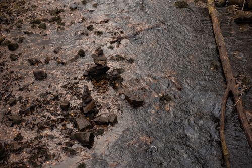 Free A tranquil stream with stacked rocks and a fallen log, epitomizing natural beauty and peace. Stock Photo