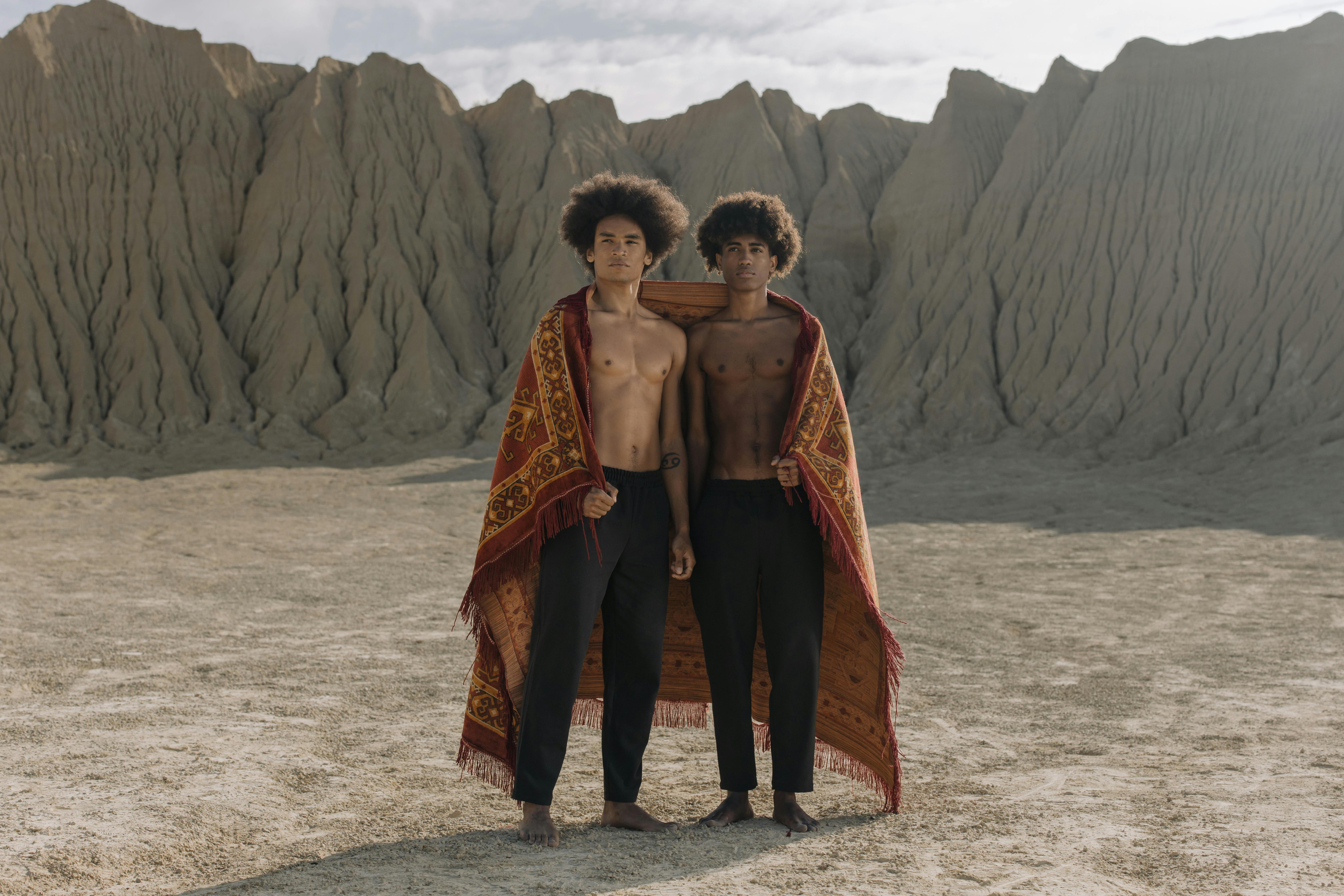 shirtless men draped with carpet in the desert