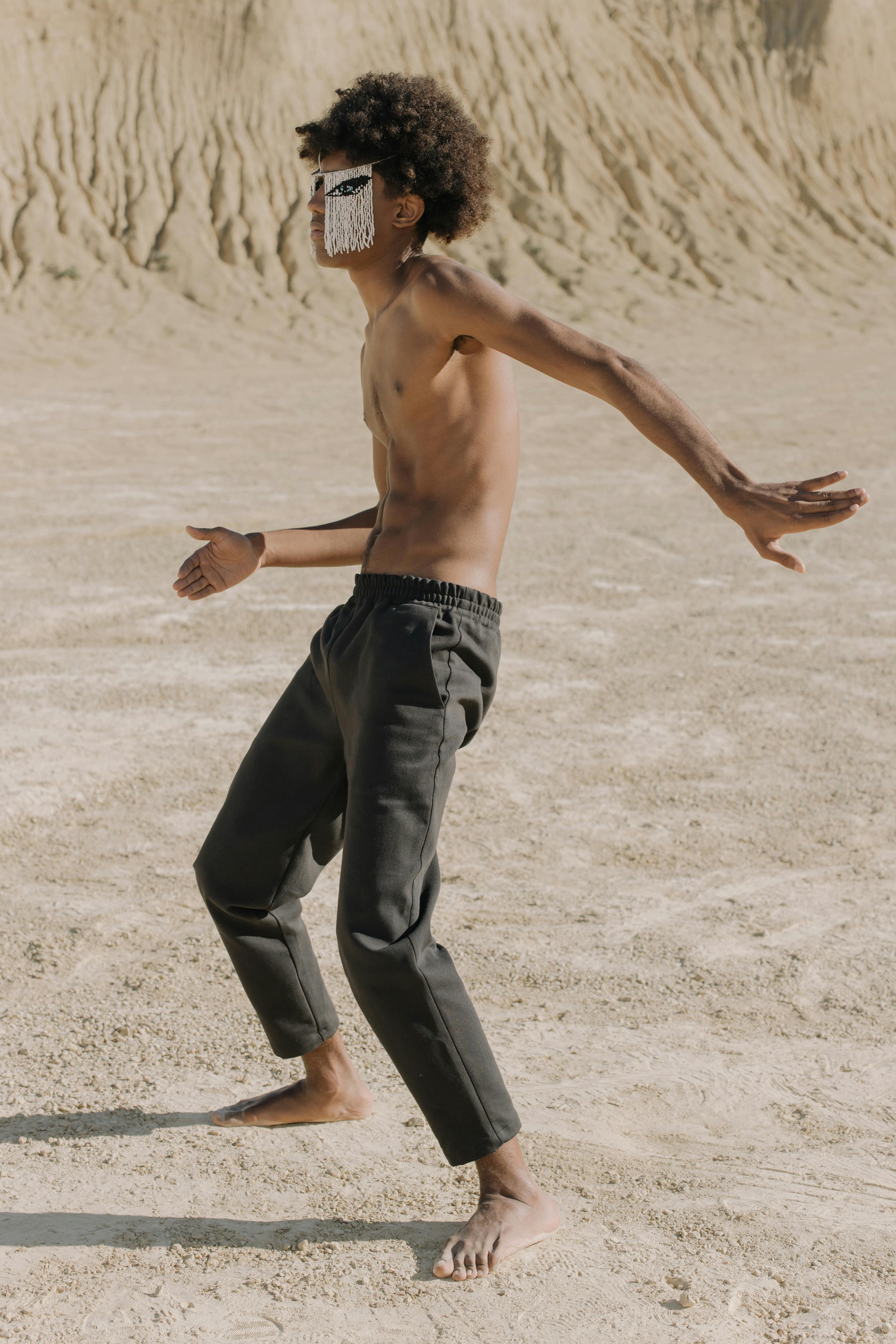 topless man in black pants walking on white sand