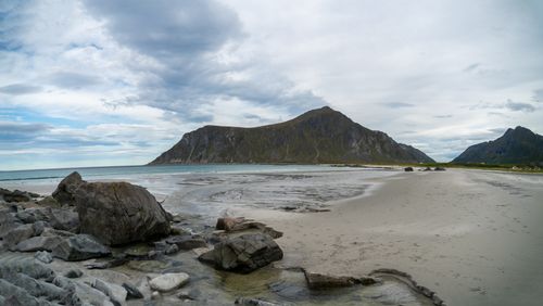 Free Wet sandy beach with stones near calm ocean and rocky cliff in distance against cloudy sky in tropical country in summer Stock Photo