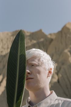 沙漠背景下，一名白发男子手持热带树叶的个人肖像