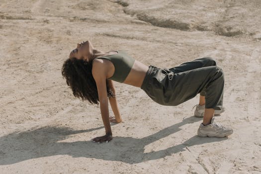 Young woman stretching and exercising on sandy outdoor terrain in athletic wear.